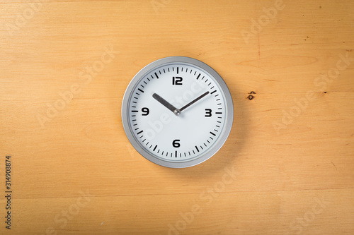 White wall clock with a yellow used hanging on the wall. Minimalist image of a wall clock on a wooden background with copy space