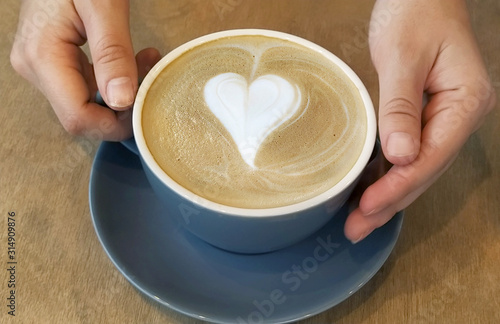 Cup of latte coffee with heart symbol on wooden background