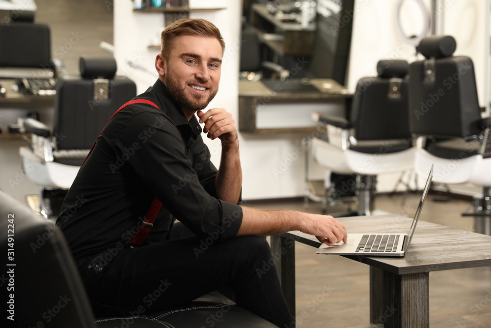 Young business owner with laptop in barber shop Young business owner with laptop in barber shop