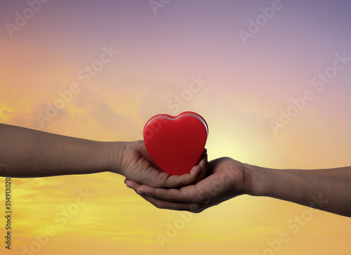 Female and man's hands with red heart at sunset