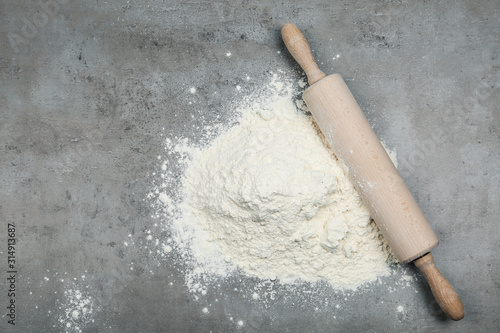 Flour and wooden rolling pin on light grey table, top view