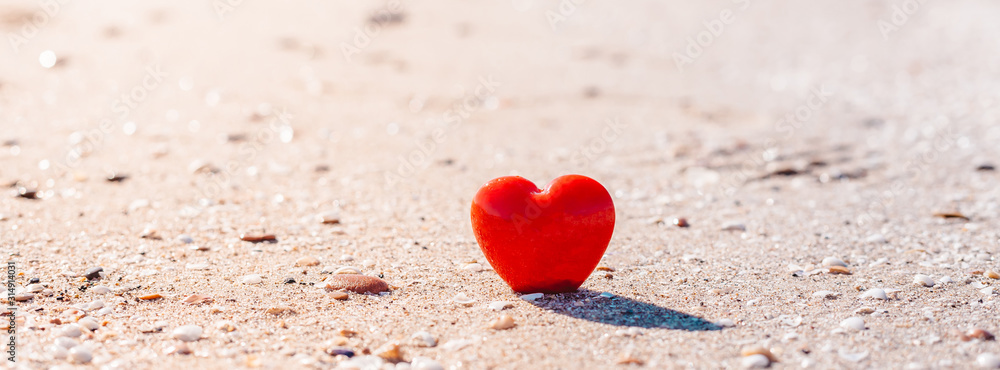 Fototapeta premium Romantic symbol of red heart on the sand beach