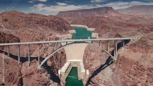 The flight over the Colorado river canyon. Crossing Hoover Dam Bypass Bridge with vehicles driving it. Coming closer to the famous Dam behind the bridge and the reservoire with turquoise water in it
