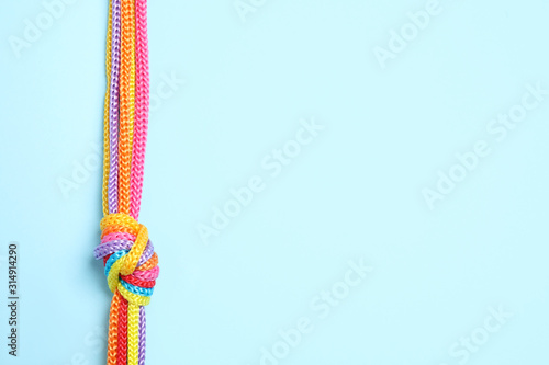 Top view of colorful ropes tied together on light blue background, space for text. Unity concept