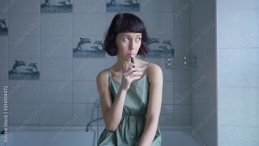 sad young caucasian brunette girl smoking electronic cigarette in bathroom alone sad young caucasian brunette girl smoking electronic cigarette in bathroom alone