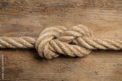 Linen rope with knot on wooden background, closeup. Unity concept