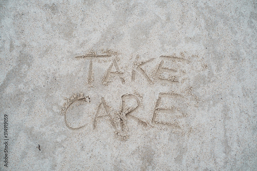 Take care sign drawn on beach sand.