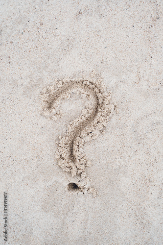 Question mark sign drawn on beach sand.