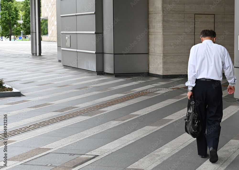 A Japanese businessman in a bent position approaches the entrance of an office building in Osaka-Japan.