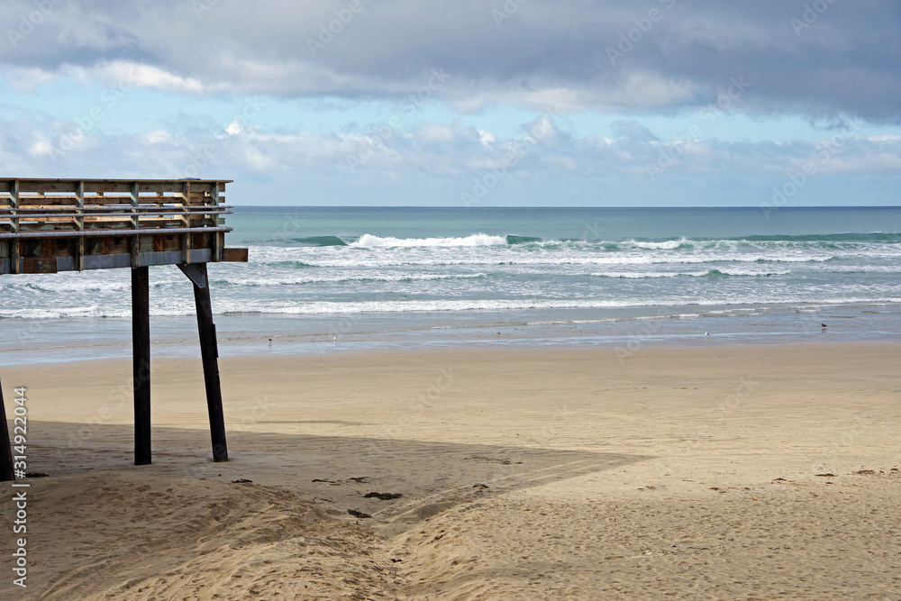 Panoramic view of an ocean beach at the California coastline with a part of a pier on the left foreground