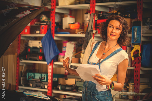 woman mechanic in blue denim overalls with a laptop and sheets of paper photo