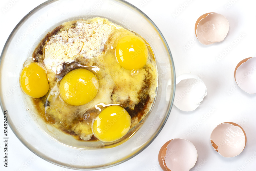 Corn and rice flour, coconut sugar, four eggs in the transparent plate. Making a cake. Mixing the dough. White background. Copy space. Place for text and design. Top view. Flat lay. Gluten-free recipe Corn and rice flour, coconut sugar, four eggs in the transparent plate. Making a cake. Mixing the dough. White background. Copy space. Place for text and design. Top view. Flat lay. Gluten-free recipe