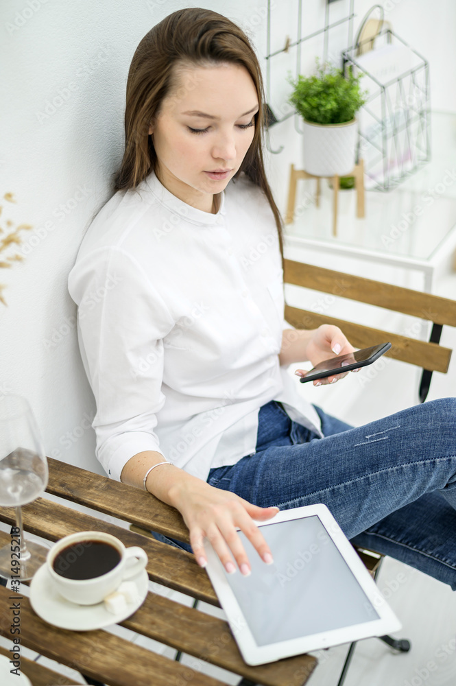 A woman in a white shirt and jeans sits in a cafe and drinks coffee. Female office worker at the lunch break talking on the phone. Manager at a business meeting in a restaurant A woman in a white shirt and jeans sits in a cafe and drinks coffee. Female office worker at the lunch break talking on the phone. Manager at a business meeting in a restaurant