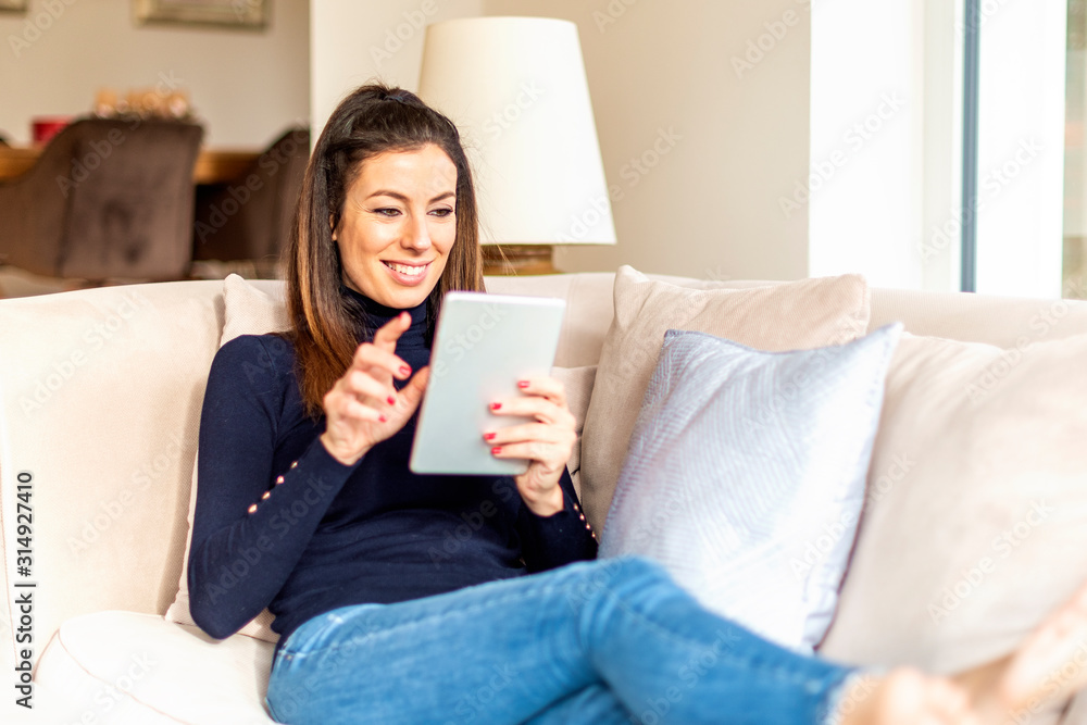 Happy woman using digital tablet while relaxing at home on the sofa Happy woman using digital tablet while relaxing at home on the sofa