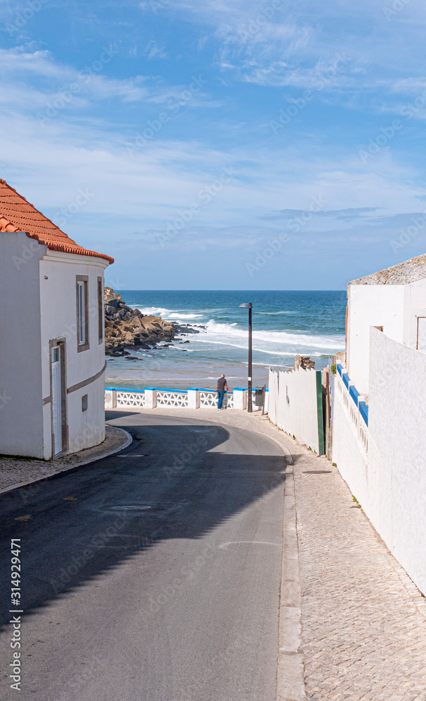 Sea view with one man leaning against a white wall, looking out to the Atlantic ocean. Taken on a sunny day in Colares, Portugal.