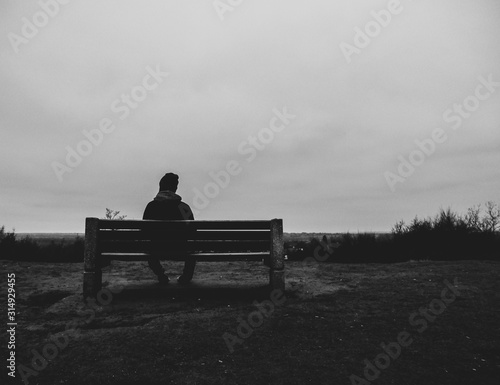 One man sitting alone on a bench on top of a hill overlooking flat countryside. Taken on a dark, overcast Autumn day in Sandy, Bedfordshire.