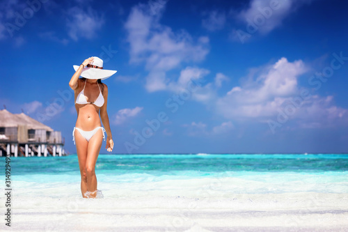 Eine schöne Frau in weißem Bikini läuft an einem tropischen Strand mit türkisem Meer und genießt den Urlaub