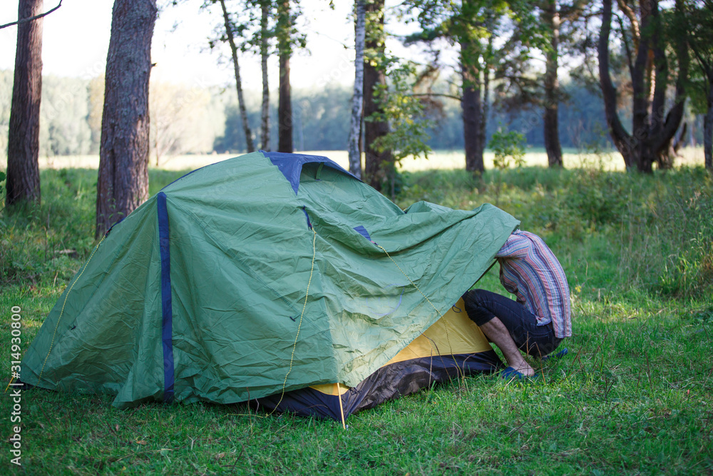 A green tourist tent stands in the forest, illuminated by rays of light. Setting up a tent in a tourist camp, tourists spending the night A green tourist tent stands in the forest, illuminated by rays of light. Setting up a tent in a tourist camp, tourists spending the night