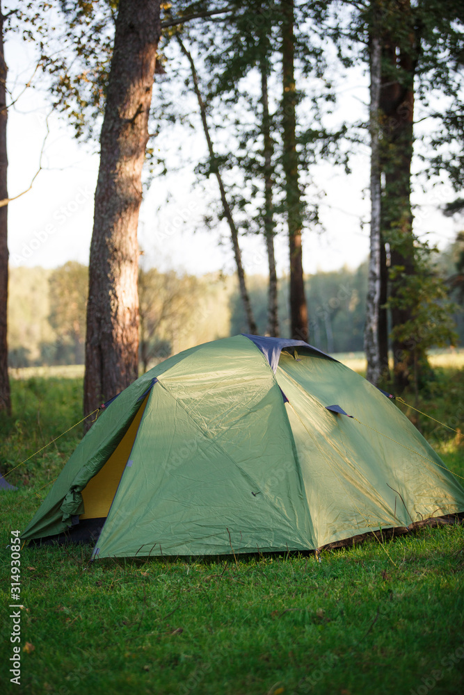 A green tourist tent stands in the forest, illuminated by rays of light. Setting up a tent in a tourist camp, tourists spending the night