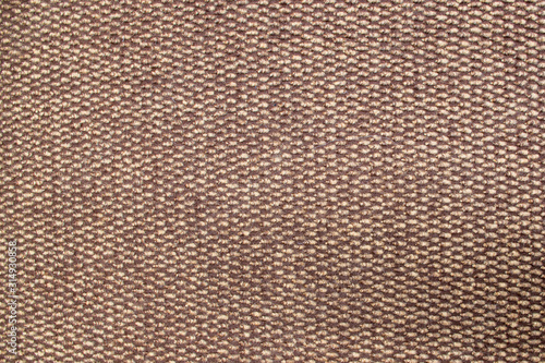 A fragment of a fluffy fleecy foot rug containing a pattern of beige and brown orderly alternating woolen details of a braided pattern with a tufted wool texture