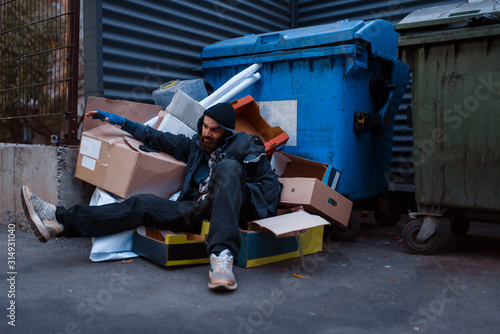 Dirty drunk beggar lies in garbage at the trashcan