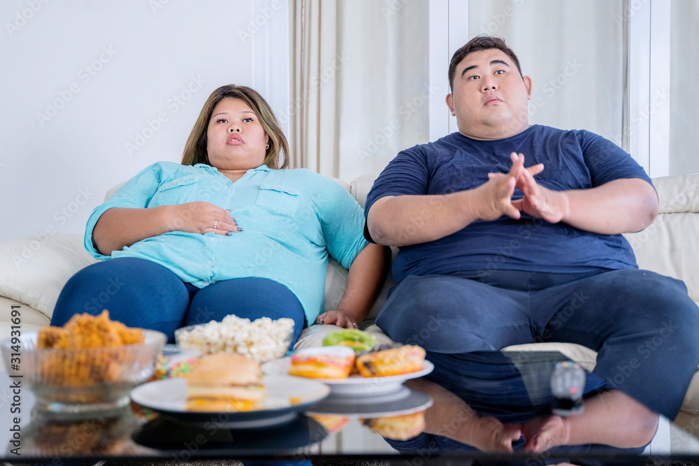 Portrait of fat couple watching tv with boredom