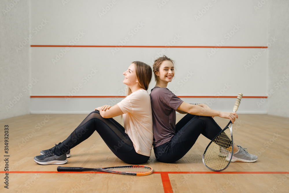 Players with squash rackets sits back to back Players with squash rackets sits back to back
