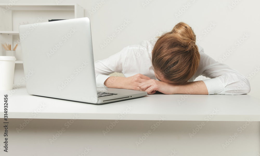Overworked and tired sleeping over a laptop in a desk at work in her office Overworked and tired sleeping over a laptop in a desk at work in her office