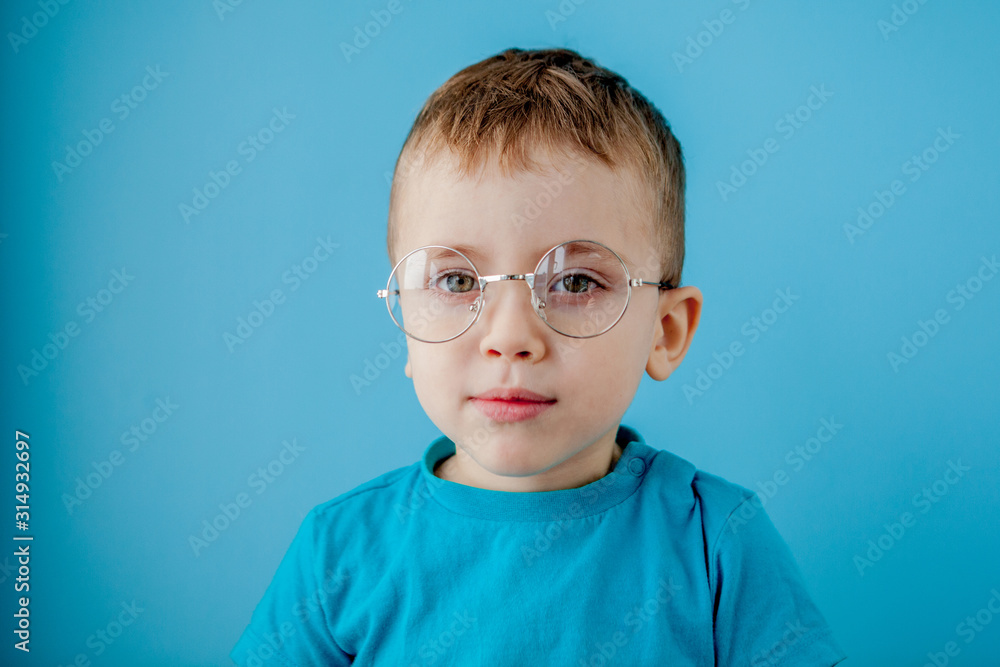 Portrait of a little smiling boy in a funny glasses. School. Preschool. Fashion. Studio portrait on a blue background, copy space Portrait of a little smiling boy in a funny glasses. School. Preschool. Fashion. Studio portrait on a blue background, copy space