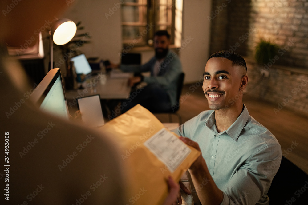 Obraz premium Happy black businessman receiving a delivery from a courier in the office.