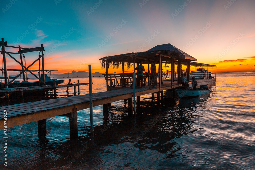 Sunset on a pier and the boat in the background on a beach on Roatan Island. Honduras