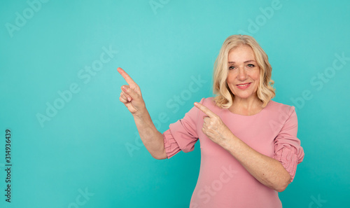 Portrait of cheerful adult woman pointing something in the blue background