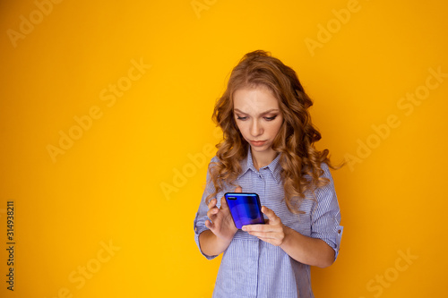Young woman using phone standing isolaed in the yelow studio