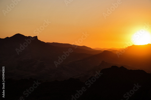 The sun sets behind the distant mountain ridges and illuminates them with its evening light.