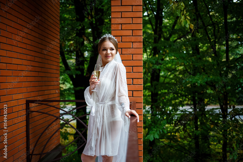 Beautiful bride in a white coat on the balcony drinks champagne from a glass Beautiful bride in a white coat on the balcony drinks champagne from a glass