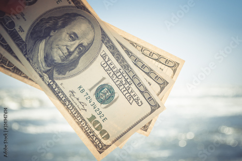 Girl holding a money bill of 300 dollars on background of sea waves