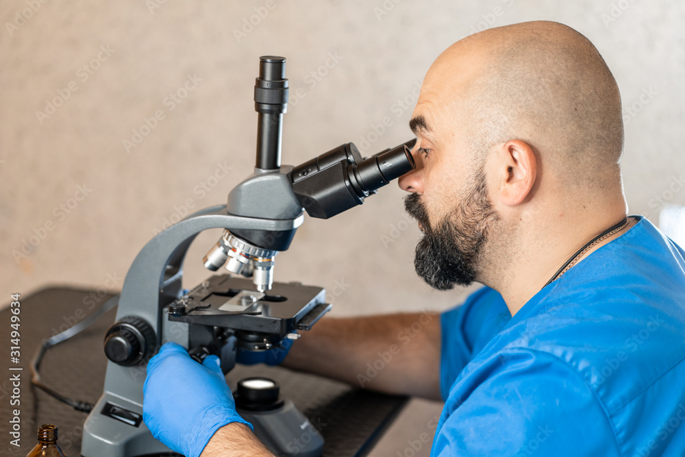 Male laboratory assistant examining biomaterial samples in a microscope Male laboratory assistant examining biomaterial samples in a microscope