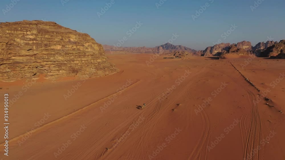 Riding camels through desert in Wadi Rum, Jordan, rising aerial view Riding camels through desert in Wadi Rum, Jordan, rising aerial view