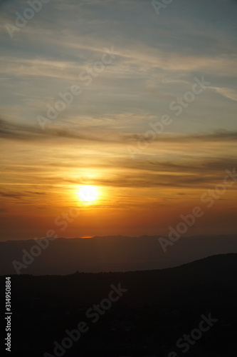 Breathtaking sunset over the sea with light reflection with a mountain range in front, dark clouds in the sky. Vertical image.