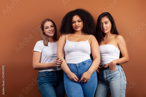 young pretty asian, caucasian, afro woman posing cheerful together on brown background, lifestyle diverse nationality people concept