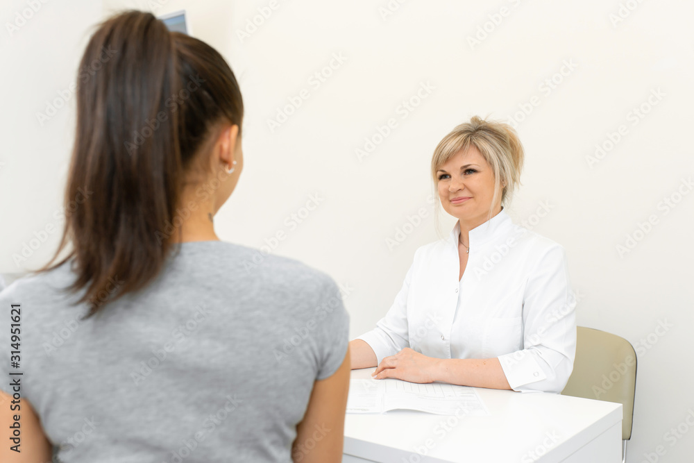 blonde doctor woman in a white coat sitting at a table in a medical office and conversation to a patient blonde doctor woman in a white coat sitting at a table in a medical office and conversation to a patient