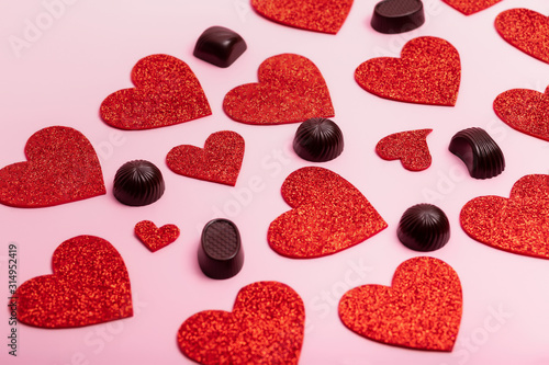 Valentine`s day poster with red hearts and chocolate candies on a pink background