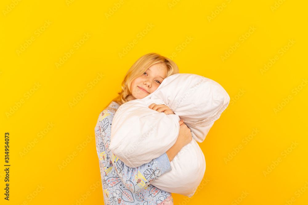 Adorable little girl looking at the camera and hugging a pillow background of a yellow wall. Adorable little girl looking at the camera and hugging a pillow background of a yellow wall.