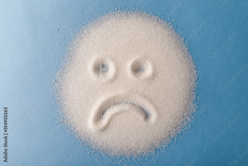 Salt scattered on black surface. Drawn sad face. Concept- diet, harm to health from excessive consumption of salt and sugar