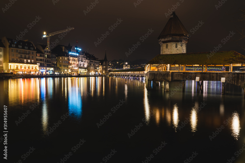 Medieval tower next to a bridge illuminated by a river at night with the lights reflected in the water