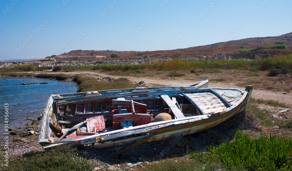 abandoned wooden fish boat at the shore. The boat is destroyed and rusty an completely useless with the sea and the blue sky at the background. Horizontal photo