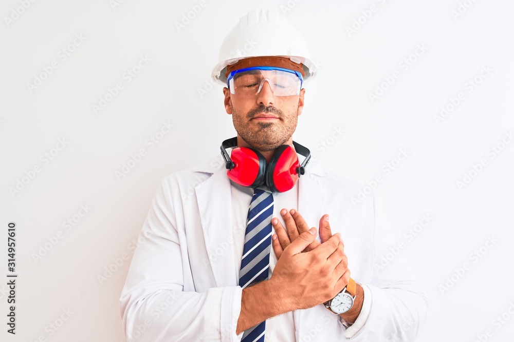 Young chemist man wearing security helmet and headphones over isolated background smiling with hands on chest with closed eyes and grateful gesture on face. Health concept.