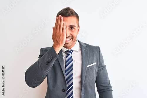 Young handsome business man wearing suit and tie over isolated background covering one eye with hand, confident smile on face and surprise emotion.