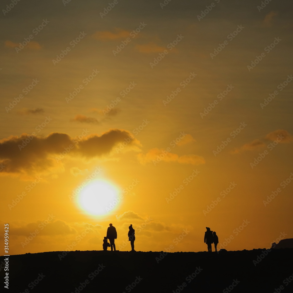 Silhouettes of people walk on horizon at sunset
