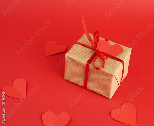 wrapped square box with a gift in brown craft paper and tied with a thin silk red ribbon